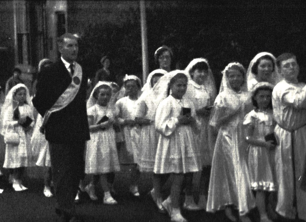 A First Holy Communion procession, probably 1950s, where children receive the Eucharist for the first time, often processing through the local streets.